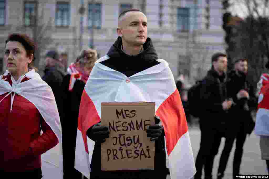 A man draped in the white-red-white flag holds a sign that reads,&nbsp;&quot;We are not your enemies.&quot; The widespread protests were met with a harsh crackdown by the government, resulting in the arrests of opposition figures and activists.