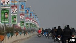 Commuters ride past election campaign posters in Rawalpindi ahead of the upcoming general elections.
