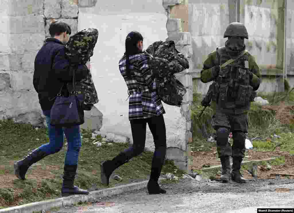Two women believed to be from the Ukrainian military carry uniforms as they leave a military base and walk past a Russian soldier on March 19. 