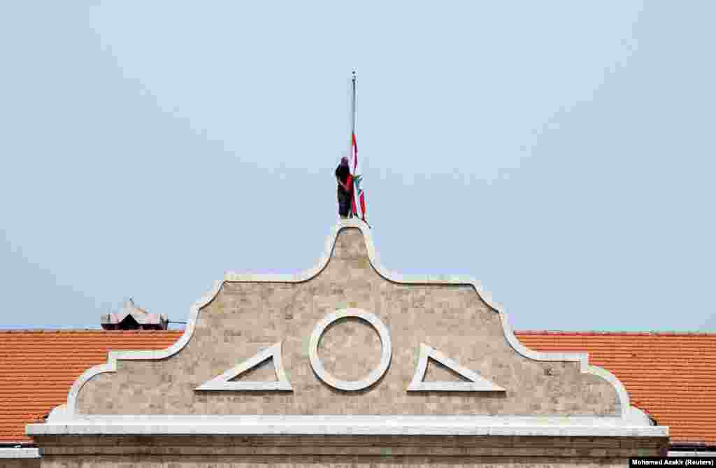 A man lowers the Lebanese national flag to half-mast outside the government palace, as caretaker Prime Minister Najib Mikati declared three days of mourning in Lebanon. 