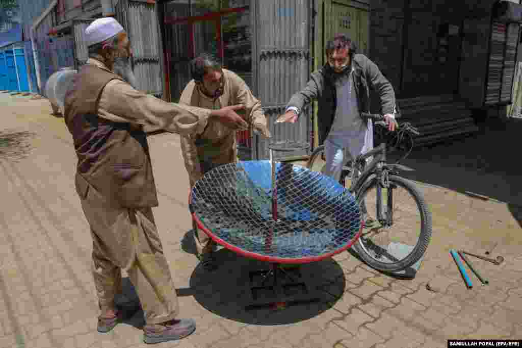 Onlookers feel the heat of the sun as Abbas (center) tests his newest stove. Proponents of solar stoves say that dishes can be prepared in the same amount of time as using a fireplace or gas stove, with the added benefit that they do not create pollution that leads to global warming. 