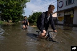 Mještani pokušavaju proći biciklom poplavljenim cestama Hersona