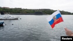 A member of Havana's Russian community held a flag as a Russian nuclear-powered submarine entered the bay of the Cuban capital in the last Russian naval visit, on June 12.