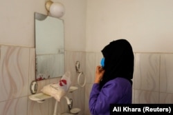 A trainee midwife arranges her head scarf in front of a mirror at a training center.