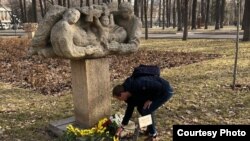 Один из участников антивоенной акции в Бишкеке, задержанный милицией, возлагает цветы к скульптуре «Наш дом - земля». 24 февраля 2023 года. 
