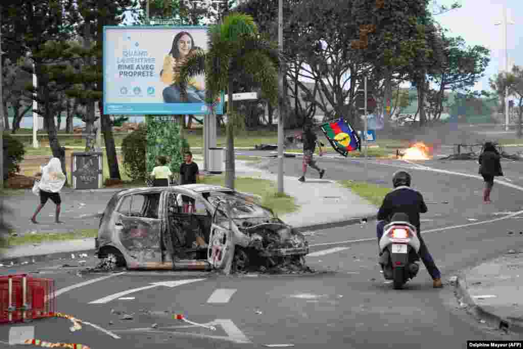 People, including a man carrying a Kanak flag, are seen as a nearby supermarket was looted in Noumea on May 14. The current unrest broke out after Paris changed New Caledonia&rsquo;s constitution to allow people who have lived in the territory for 10 years or more to vote. Kanak leaders have accused Paris of seeking to dilute the democratic power of the indigenous population.&nbsp; &nbsp;