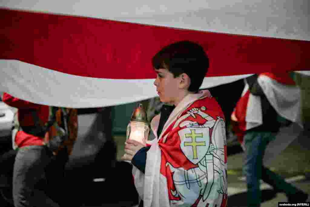A young child holds a candle as he walks beside the flag that has become a symbol of Belarusian national identity and independence.