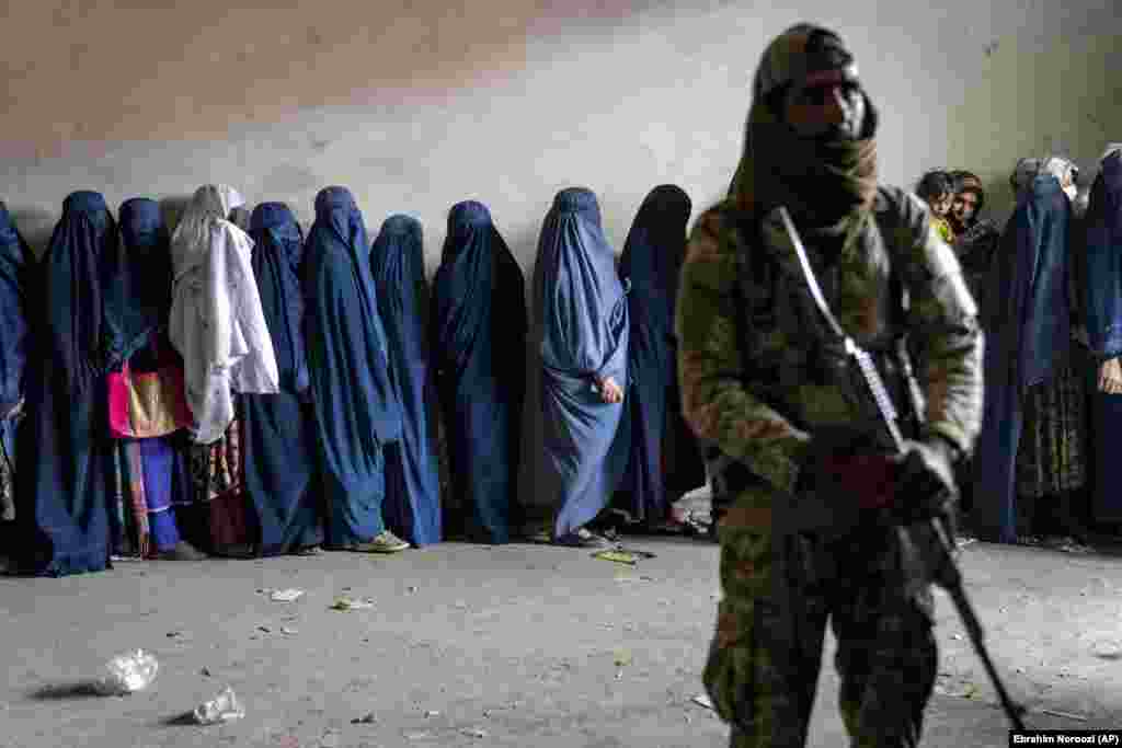 Talyban söweşijisi, ynsanperwer kömek topary tarapyndan paýlanan azyk önümlerini almak üçin garaşýan zenanlara garawullyk edýär, Kabul, Owganystan, 23-nji maý, 2023. (AP suraty/Ebrahim Noroozi)