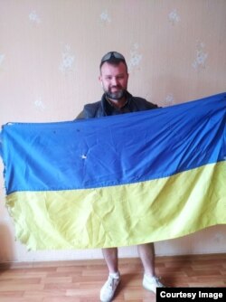 French teacher and student media center director Ivan Shybkov with the Ukrainian flag he recovered from the damaged Harant school building in Lysychansk