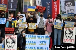 Taýbeýdäki rus wekilhanasynyň daşynda Russiýanyň Ukraina basyp girmegine garşy protest geçirilende, plakat tutup duran adamlar. 2022-nji ýylyň 1-nji marty.