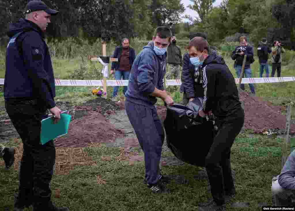 A police officer looks on as men carry the body of a person who, according to Ukrainian police, was killed by Russian troops in Balaklia. 