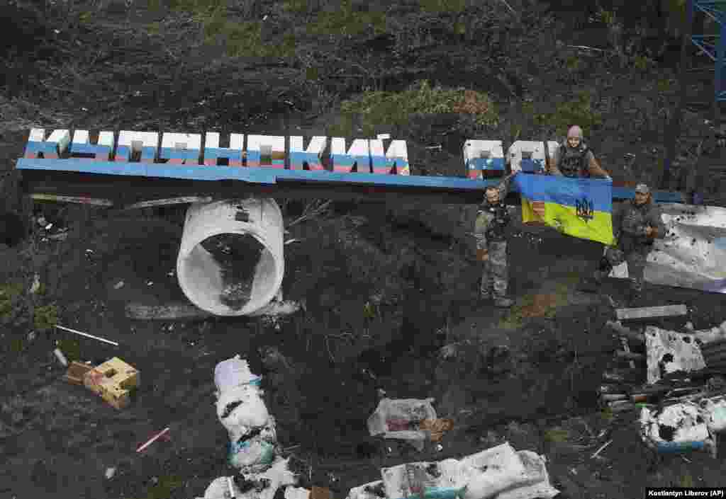 Ukrainian soldiers proudly show their national flag near the damaged "Kupyansk district" sign in the Kharkiv region.
