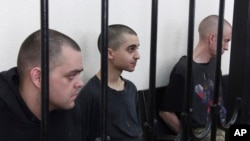 British citizens Aiden Aslin (left) and Shaun Pinner (right), along with Moroccan Saaudun Brahim (center), sit behind bars in a courtroom in Donetsk, eastern Ukraine, on June 9.