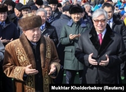 Öňki prezident Nursoltan Nazarbaýew (çepde) we prezident Kasym-Žomart Tokaýew bilen bilelikde Astanada Nowruz baýramy mynasybetli gurlan söwda merkezinde doga-töwir edýärler. Astana, 2019-njy ýylyň 21-nji marty. Üç ýyldan soň Tokaýew Nazarbaýewi "elbasy" hormatly adyndan mahrum etdi.