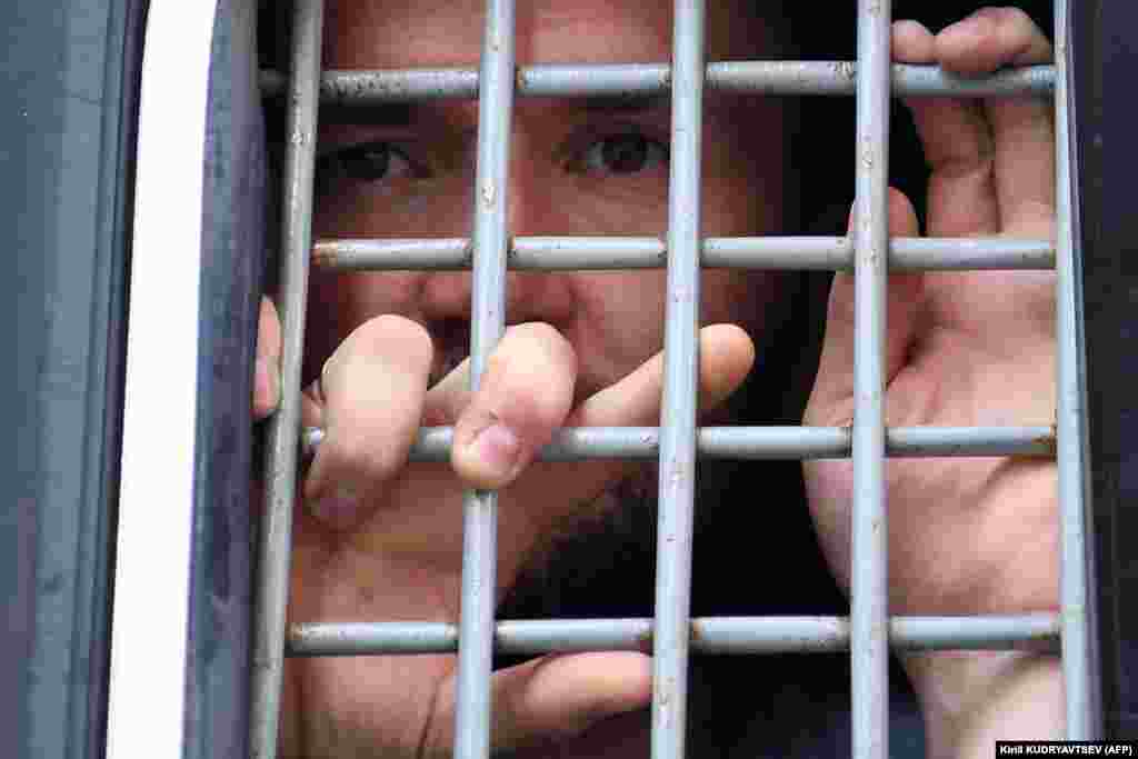 A detained protester looks out from the barred window of a police van. 