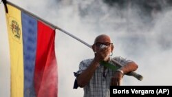 An opponent of President Nicolas Maduro carrying a Venezuelan flag covers his face amid tear gas fired by soldiers loyal to Maduro during an attempted military uprising to oust Maduro in Caracas on April 30.