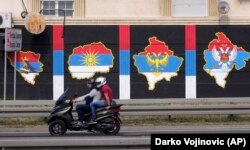 A motorbike passes a mural depicting (from left) the maps of Bosnia, North Macedonia, Kosovo, and Montenegro painted in the colors of the Serbian flag, in Belgrade on August 26.