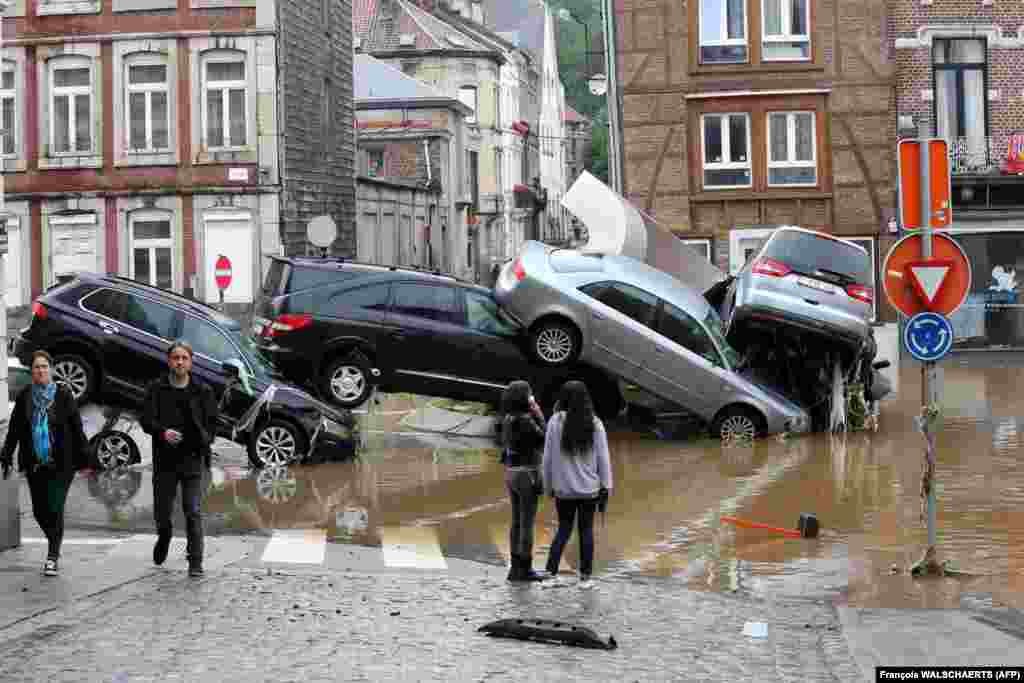 O fotografie făcută la 15 iulie arată oameni care treceau pe lângă mașiniile aduse de viitură la un sens giratoriu din orașul belgian Verviers, după ce ploile abundente și inundațiile au lovit vestul Europei, ucigând cel puțin două persoane în Belgia.