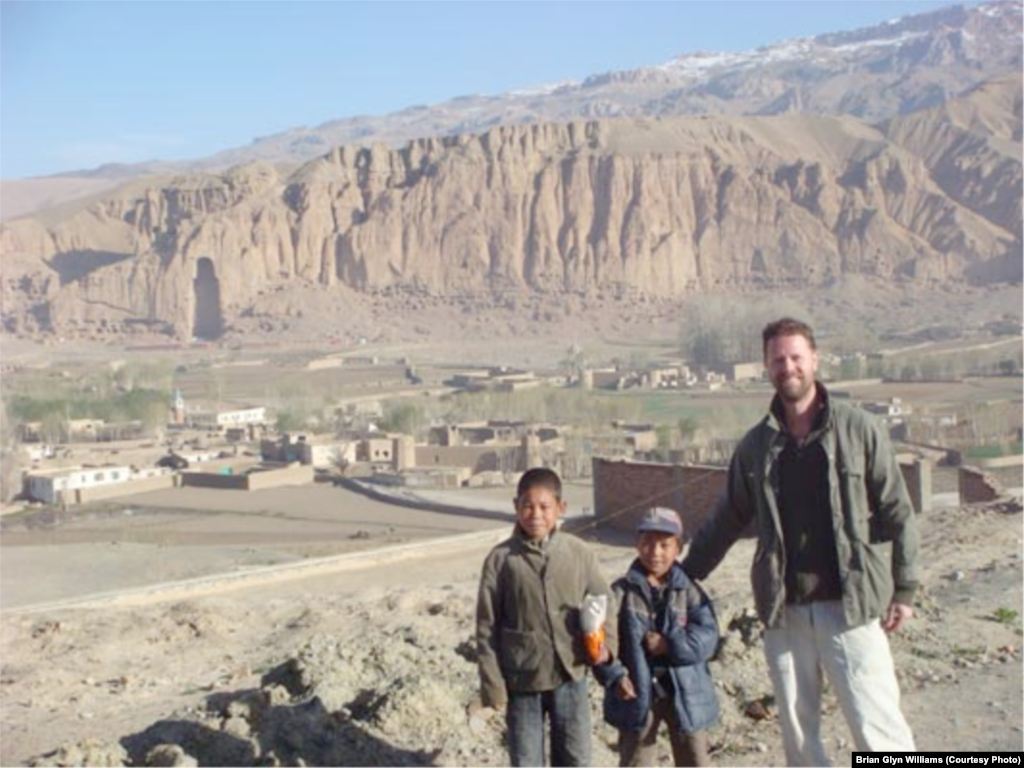 With Hazara children in the Vale of Bamiyan located at 8,000 feet in the remote Hindu Kush Mountains. In the background is an empty niche in the rock face where Afghanistan’s most famous historic monument, one of two magnificent 6th-century carvings of Buddha, once stood. The two giant stone carvings were blasted to rubble by the Taliban in March 2001 after the hard-line Islamists labeled them a “pagan idol.”