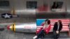 Două chinezoaice stau pe o bancă pictată cu drapelul american în fața unui magazin din Beijing, 23 martie 2018 (AP Photo/Ng Han Guan)
