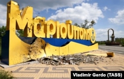 The damaged entrance sign to the city of Mariupol and the monument to Metropolitan Ignatius of Mariupol