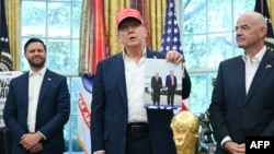 Donald Trump, flancat de vicepreședintele american JD Vance (stânga) și președintele FIFA, Gianni Infantino, ține în mână o fotografie cu el și președintele rus Vladimir Putin în Alaska, în timp ce vorbește în Biroul Oval al Casei Albe, la Washington, DC, pe 22 august 2025.