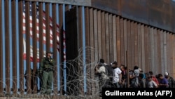 Migranți din țări din America Centrală se uită prin gardul de la frontiera cu Mexic, lângă punctul de trecere El Chaparral, Baja, California