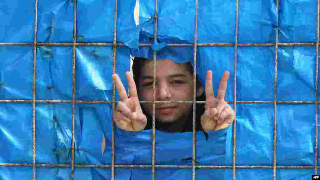 A young Syrian refugee flashes the "peace" sign from behind a fence at a refugee camp in Yayladagi, Turkey.