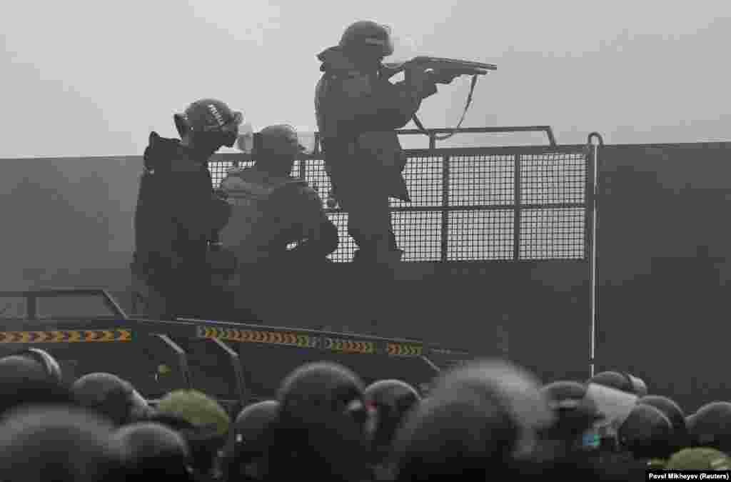 A Kazakh riot policeman aims a weapon at protesters from a barricade in Almaty. 