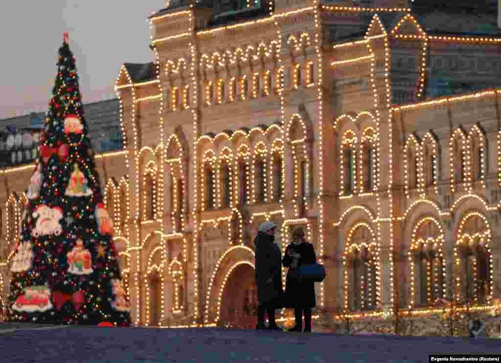 Woman stand beside an ornamented tree in front of Moscow&#39;s GUM department store, which is illuminated for the New Year&#39;s and Christmas season.&nbsp;Russians routinely refer to decorated seasonal conifers as &quot;New Year firs&quot; or &quot;New Year spruces,&quot; a legacy from the Soviet era when religious symbols were frowned upon.