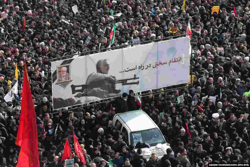 Iranian mourners carry a huge banner showing the image of Qasem Soleimani with the slogan "hard revenge is on the way."