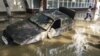 A local resident passes by a damaged car stuck in a flooded street in the town of Krymsk in Russia's Krasnodar region.