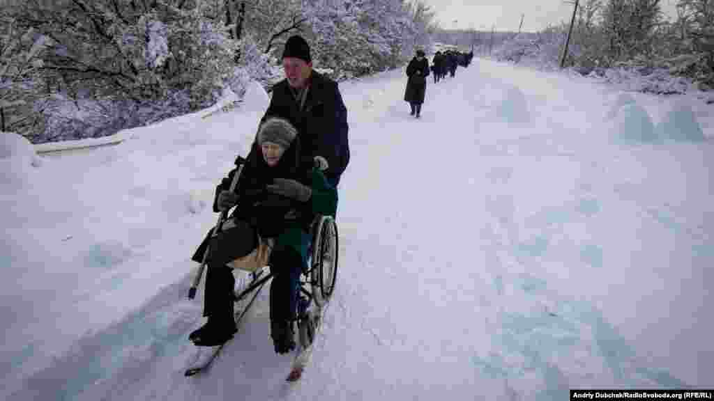 An elderly woman being pushed on her winter-modified wheelchair. 