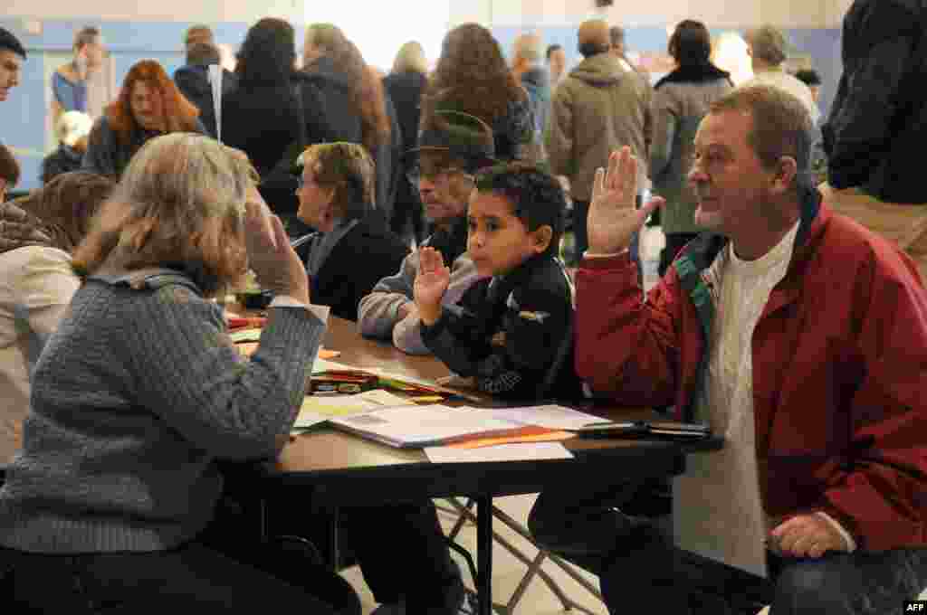 Tom Hoisington (right) raises his right hand after being registered to vote at the Bishop Leo O'Neil Youth Center in Manchester, New Hampshire. Hoisington's grandson, Tonykus Hebert, mimics his grandfather.