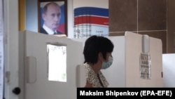 With a portrait of President Vladimir Putin in the background, a woman in Moscow prepares to cast her ballot during early voting in a controversial plebiscite on amendments to the Russian Constitution. 